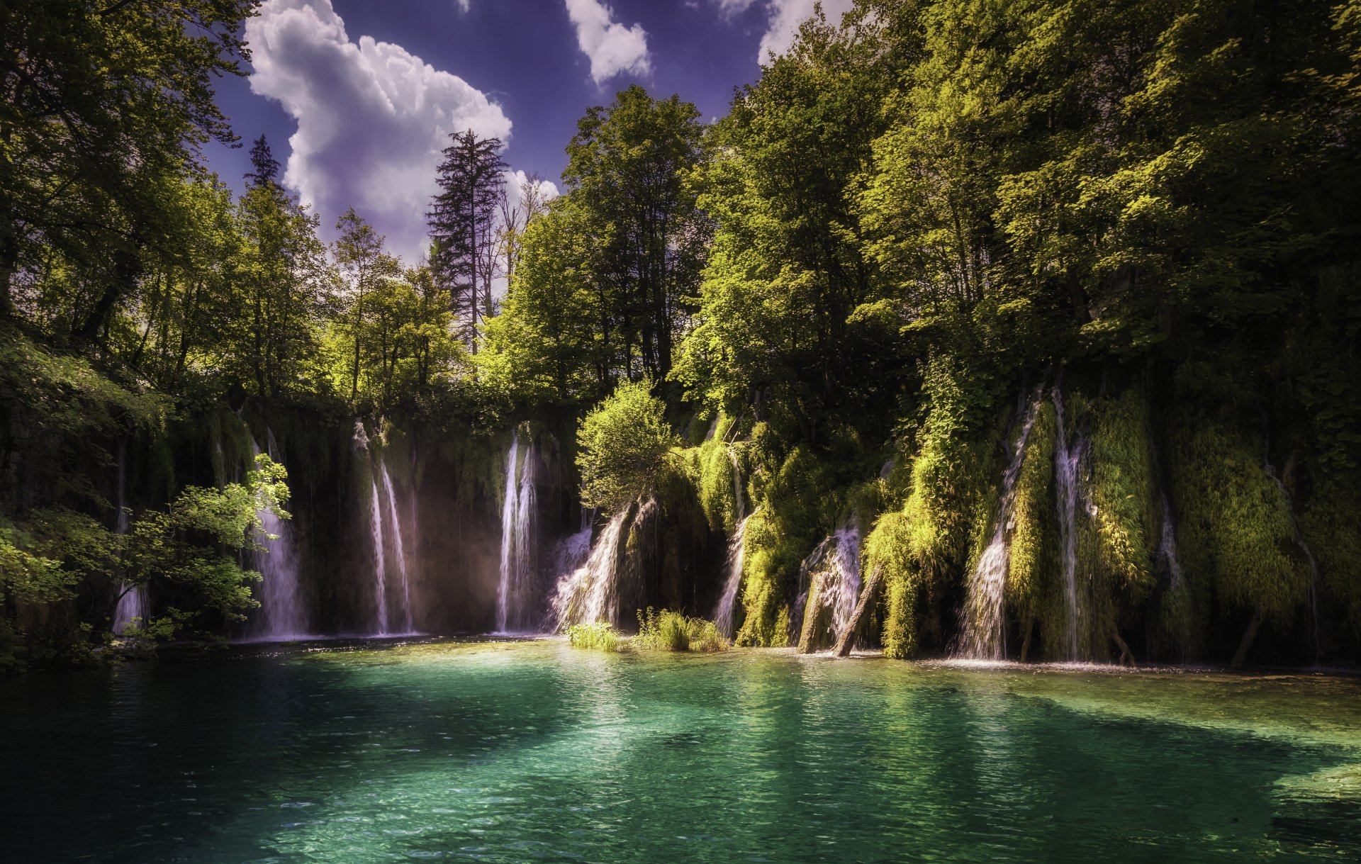 Croatia nature scene: cascading waterfalls into a turquoise lake surrounded by mossy cliffs and forest under a dramatic sky — 2K Quad HD PC desktop wallpaper/background.