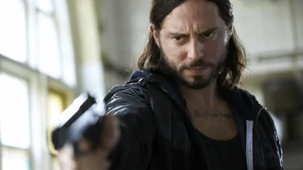 A tense scene from the TV show Snabba Cash, featuring a man aiming a gun with a serious expression, set against a dimly lit interior backdrop. HD wallpaper quality.