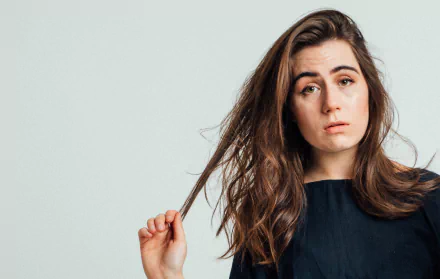 A high-definition desktop wallpaper featuring Dodie, showcasing her thoughtful expression and long, wavy hair against a light background, capturing the essence of her music.