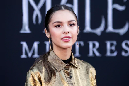 HD wallpaper of American brunette singer and actress Olivia Rodrigo with a sleek hairstyle, wearing a metallic gold outfit against a dark background.