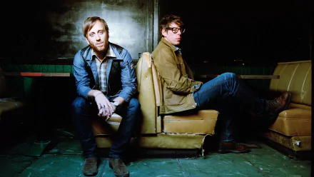 HD wallpaper featuring two band members sitting back-to-back in vintage interior, evoking The Black Keys' style.