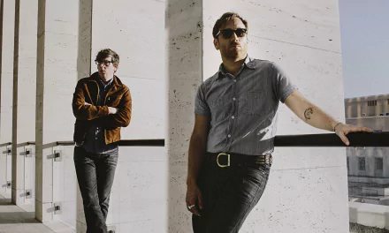 Two members of The Black Keys band posing casually, one leaning against a railing and the other standing in the background, in a high-definition desktop wallpaper.
