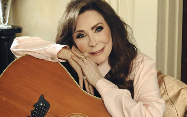 A stunning HD desktop wallpaper featuring Loretta Lynn, showcasing her iconic presence as she smiles while resting her chin on her hand beside her guitar.