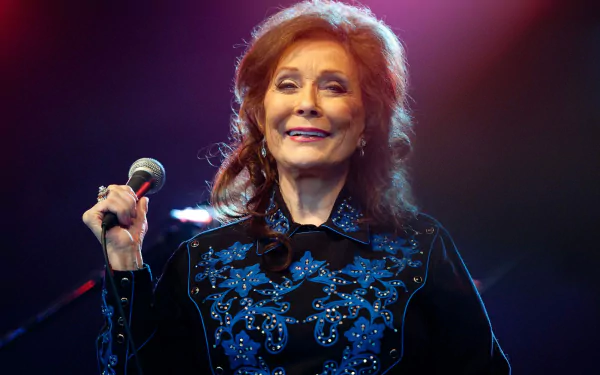 HD desktop wallpaper featuring a smiling woman with a microphone, tagged as Loretta Lynn, with a blue-lit stage background.
