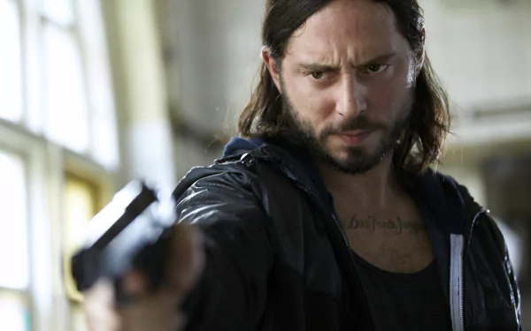 A tense scene from the TV show Snabba Cash, featuring a man aiming a gun with a serious expression, set against a dimly lit interior backdrop. HD wallpaper quality.