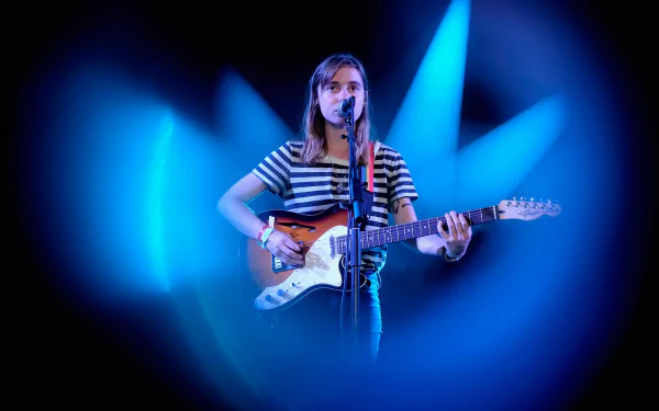 HD desktop wallpaper of a musician with a guitar highlighted by blue stage lights, providing an atmospheric background.