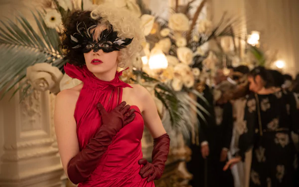 4K Ultra HD desktop wallpaper: woman in a red gown and black feather mask posing at a lavish floral ball, cinematic styling inspired by the movie Cruella.