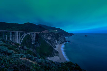 4K Ultra HD wallpaper of Bixby Creek Bridge spanning a rocky coastline with a beach below under a vibrant blue sky.