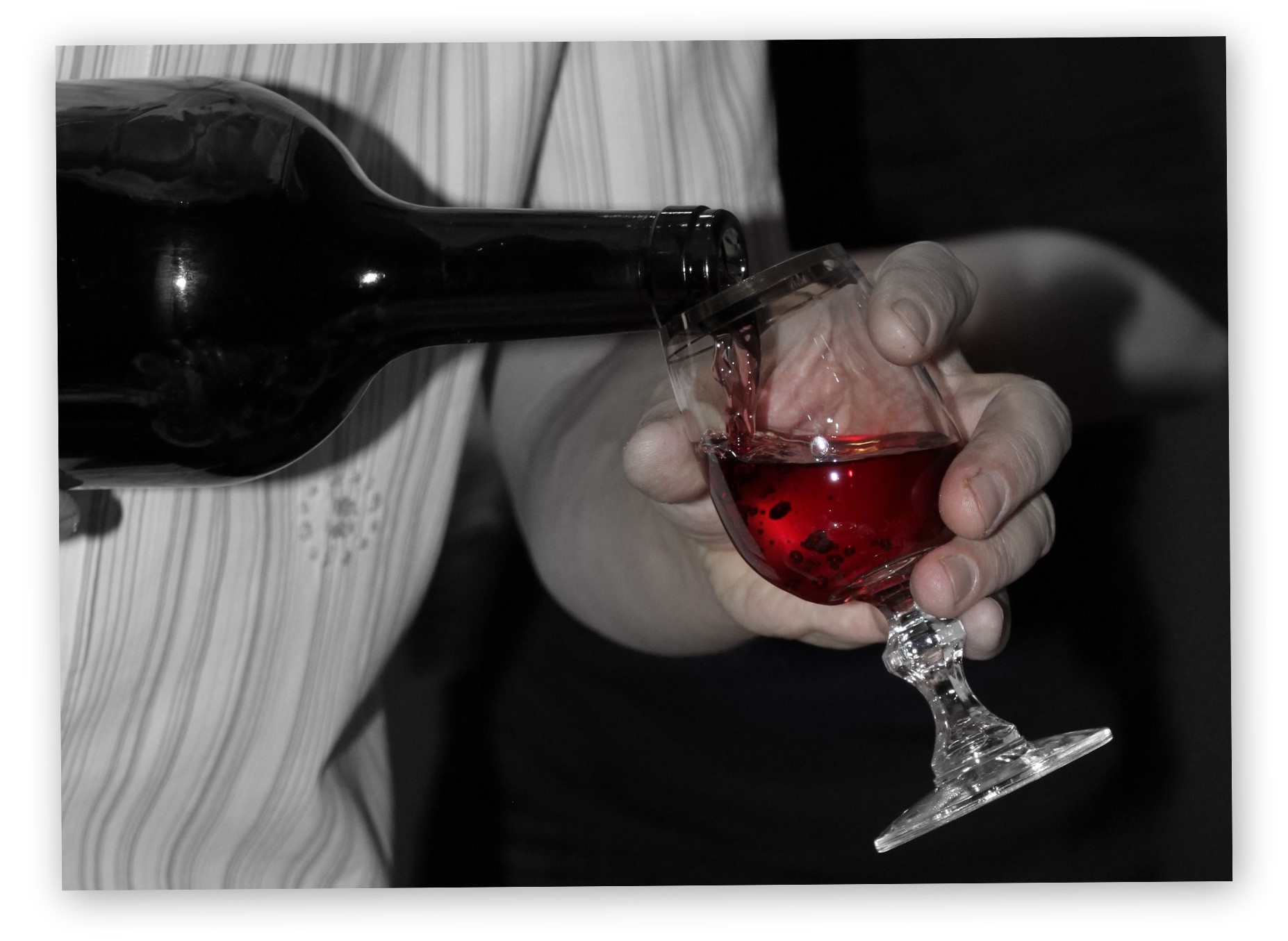 Glass of red wine on a black and white background with a bottle nearby.