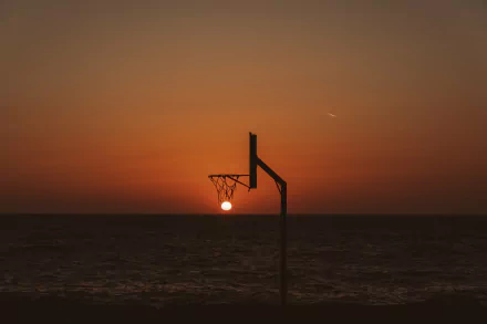 A basketball hoop silhouetted against a vibrant sunset over the ocean, captured in stunning 4K Ultra HD photography for a striking PC desktop wallpaper.