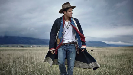 Man in cowboy hat and stylish western attire standing in open field under cloudy sky, HD desktop wallpaper and background.
