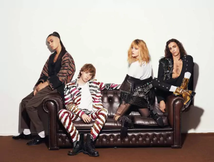 Band members posing stylishly on a brown leather couch with a white backdrop for a HD Maneskin desktop wallpaper.