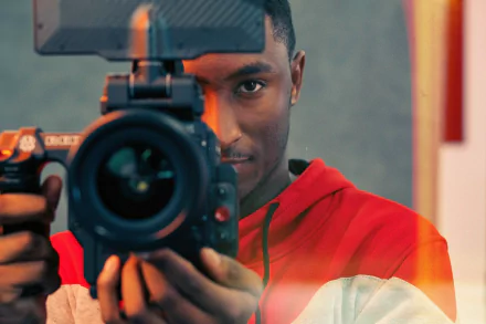 A man in a red hoodie holding a camera, serving as an engaging HD wallpaper with a creative vibe.