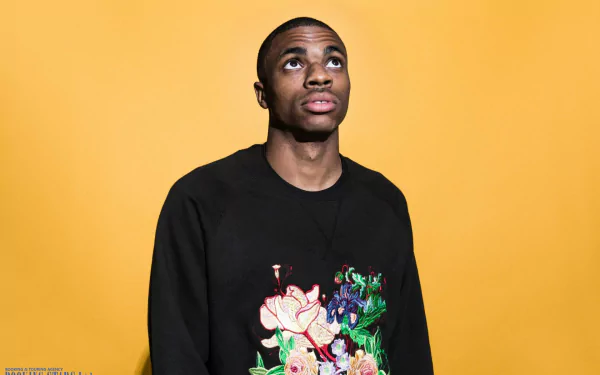 Man in black sweatshirt with floral design looking upwards against a yellow background, HD desktop wallpaper.