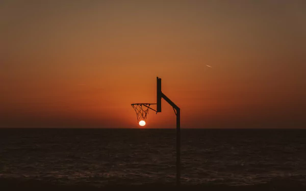 A basketball hoop silhouetted against a vibrant sunset over the ocean, captured in stunning 4K Ultra HD photography for a striking PC desktop wallpaper.