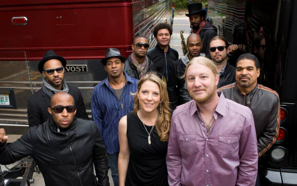 A vibrant group portrait of the Tedeschi Trucks Band, showcasing musicians in stylish outfits, standing confidently in front of a tour bus, capturing the essence of their music.