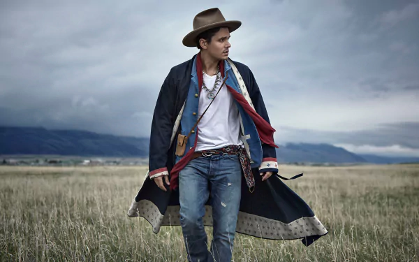 Man in cowboy hat and stylish western attire standing in open field under cloudy sky, HD desktop wallpaper and background.