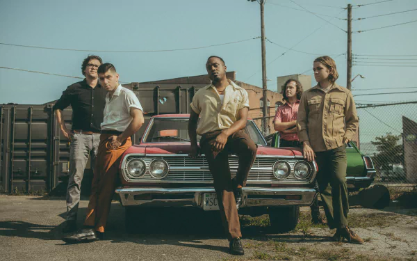 HD desktop wallpaper featuring members of the band Durand Jones & The Indications posed in front of a vintage car with an urban backdrop.