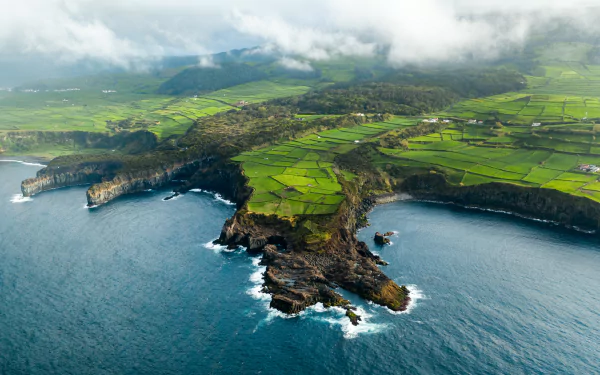 Aerial view of a rugged coastline with cliffs and patchwork green fields under low clouds — 4K Ultra HD PC desktop wallpaper and background, nature coastline.