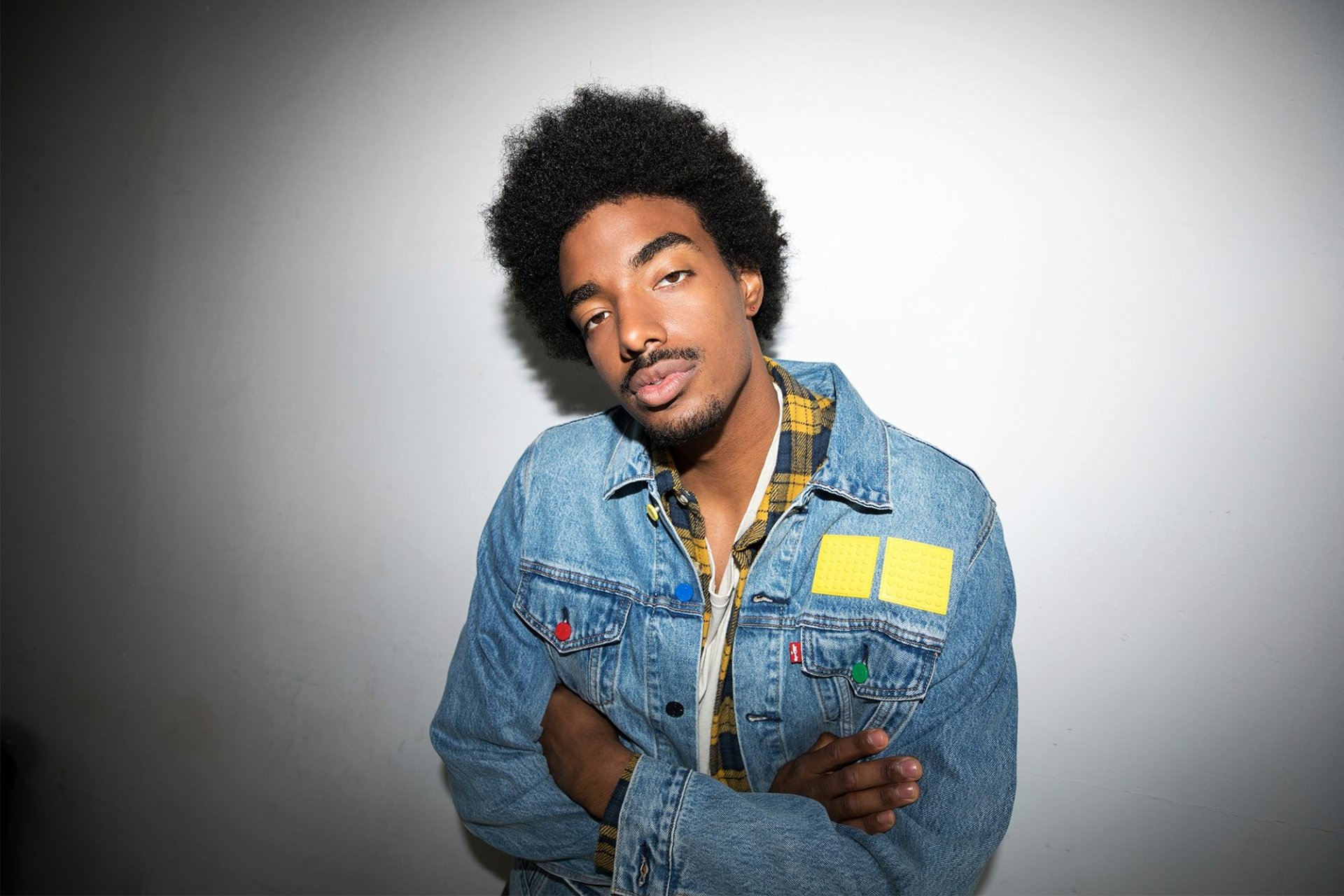 Stylish individual in a denim jacket posing with a confident smile for an HD desktop wallpaper and background.