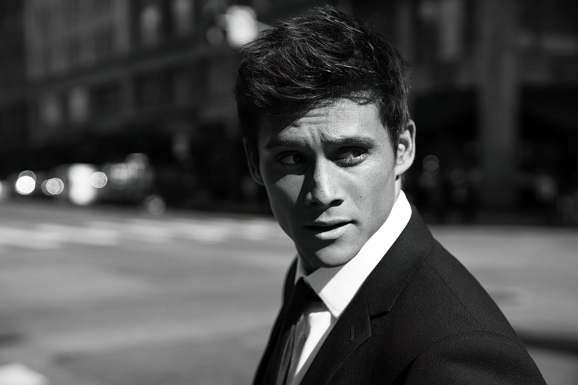 Black and white HD desktop wallpaper featuring a stylish man in a suit looking over his shoulder on a city street.