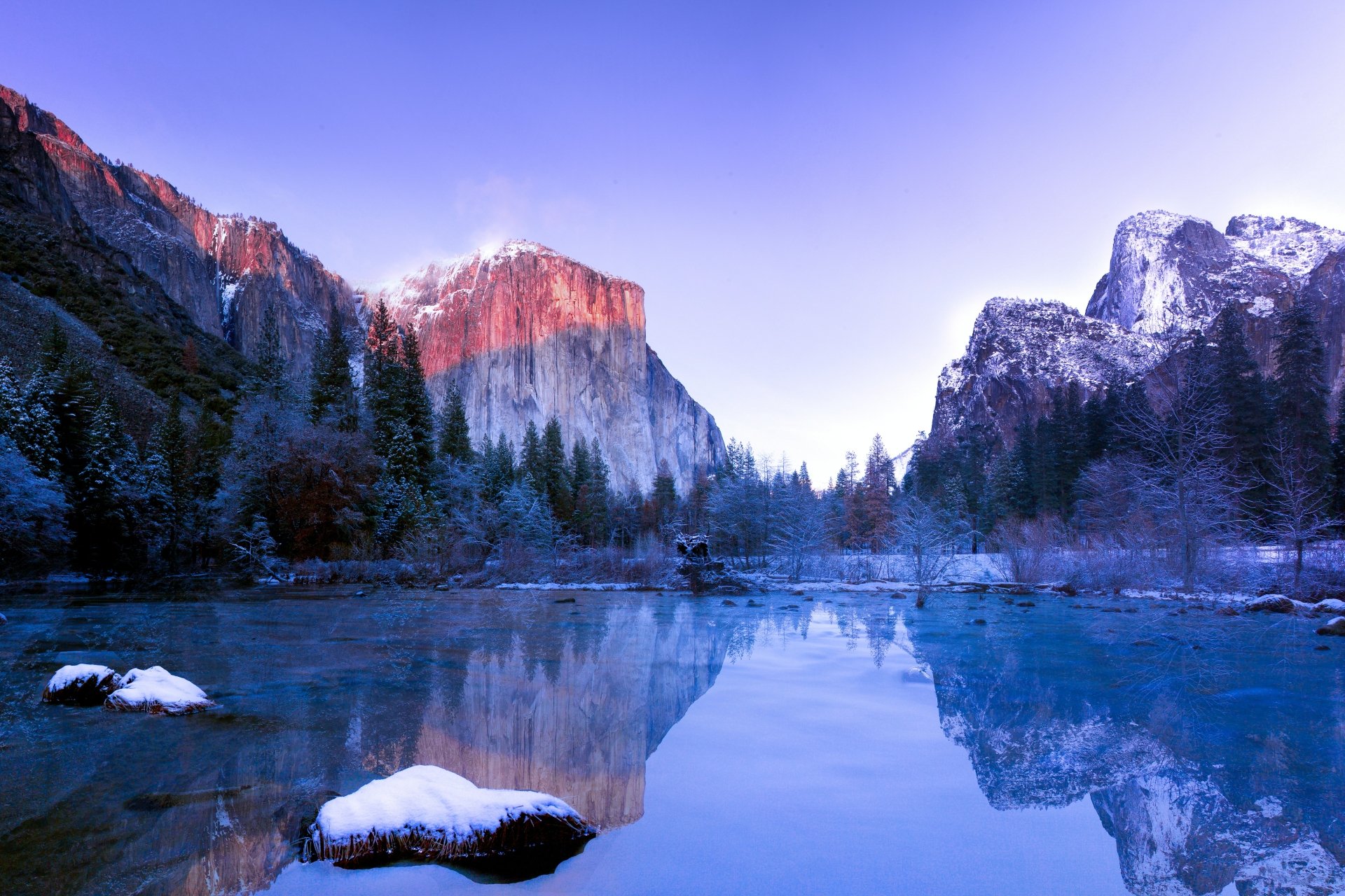 A serene lake in Yosemite National Park reflects surrounding snow-capped mountains and pine trees under a clear sky, captured in stunning 4K Ultra HD detail.