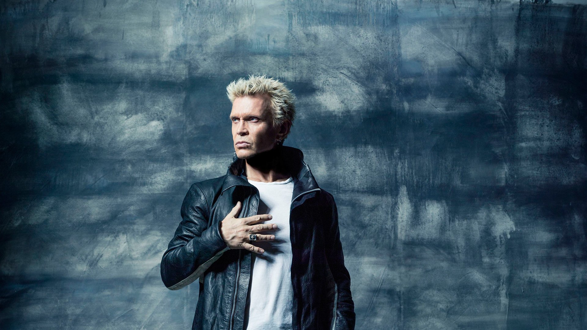 Billy Idol poses confidently against a textured blue background, showcasing his iconic style. This HD wallpaper captures the essence of music and rock culture seamlessly.