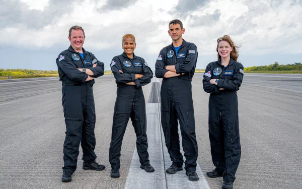 HD wallpaper featuring the Inspiration4 mission crew in flight suits, standing confidently on a runway with a cloudy sky in the background.