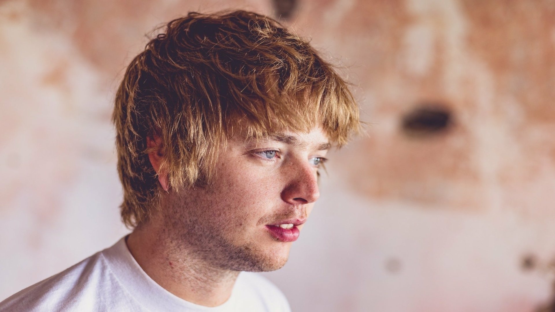 HD desktop wallpaper featuring a profile view of a pensive man with blonde hair against a subtle textured backdrop.