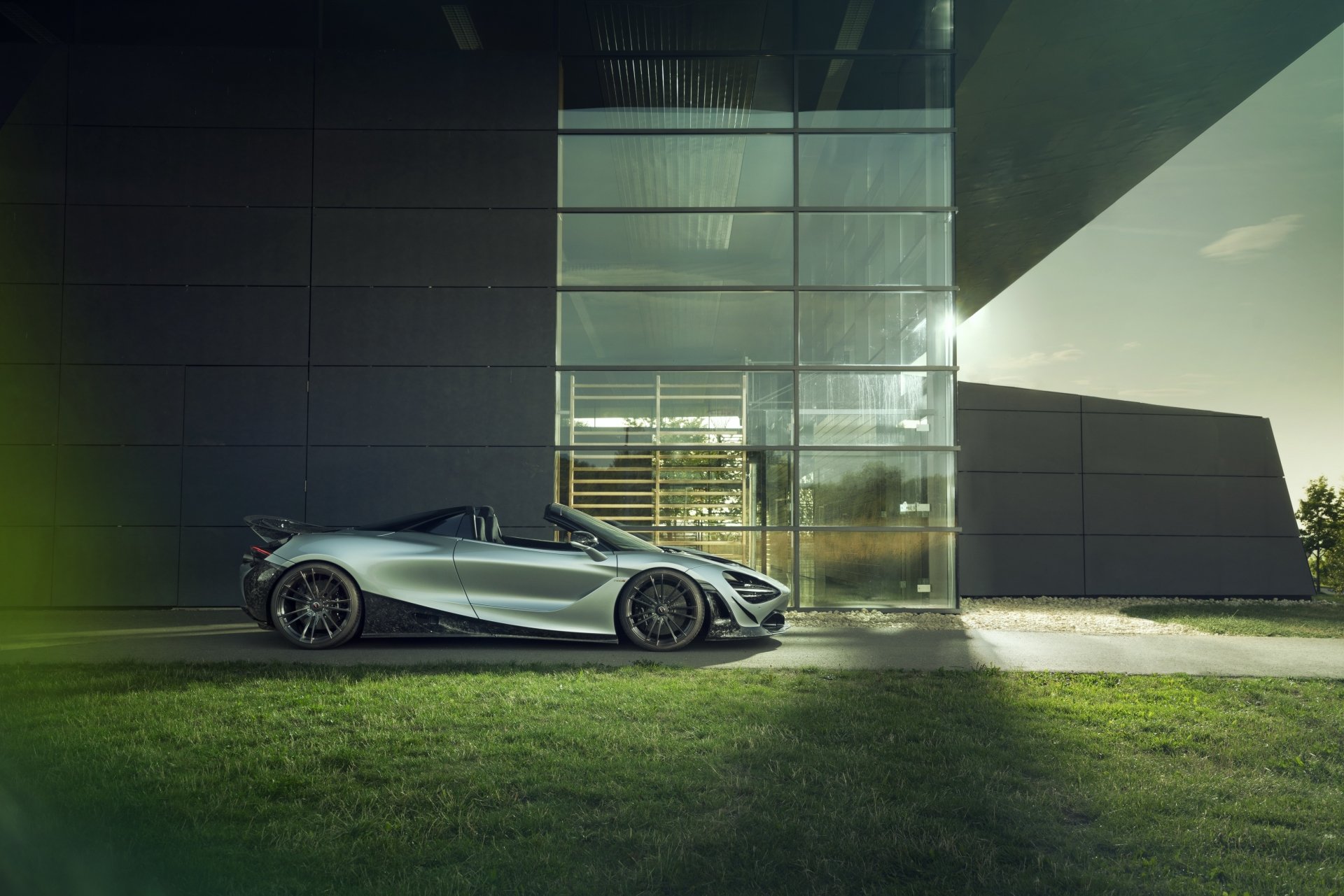 Silver McLaren 720S supercar parked beside a modern glass building on a lawn at dusk — 4K Ultra HD PC desktop wallpaper.