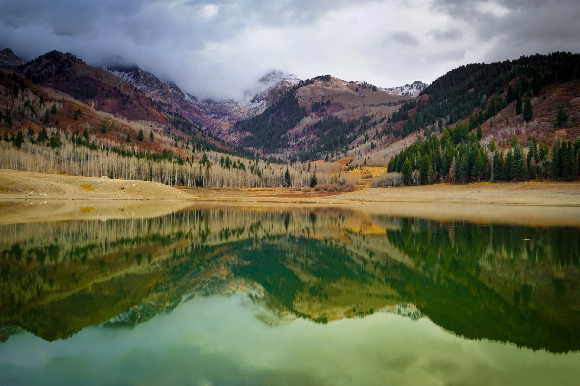 4K Ultra HD PC desktop wallpaper: Utah mountain lake mirroring autumn-colored slopes and evergreen forests under a moody, cloud-veiled sky.