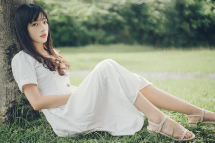 4K Ultra HD PC desktop wallpaper: young woman in a white dress reclining against a tree on a sunlit grassy field.