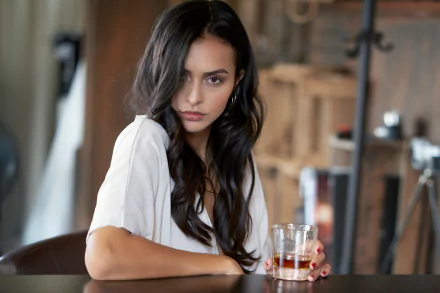4K Ultra HD PC desktop wallpaper: black‑haired woman model with long waves, seated at a bar holding a glass, intense gaze, soft natural light and blurred background.