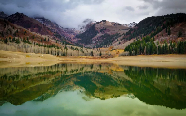 4K Ultra HD PC desktop wallpaper: Utah mountain lake mirroring autumn-colored slopes and evergreen forests under a moody, cloud-veiled sky.