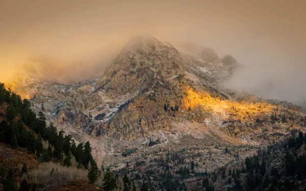 HD PC desktop wallpaper showcasing Utah’s rugged mountain landscape with mist and warm sunlight illuminating rocky peaks and forested slopes.