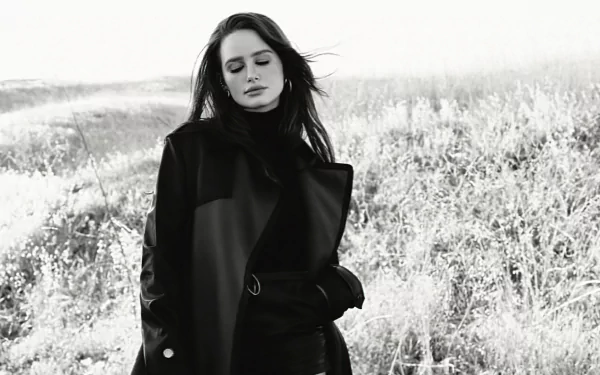Black-and-white HD PC desktop wallpaper of a female celebrity in a long coat standing in a windswept field, gazing downward with a contemplative expression.