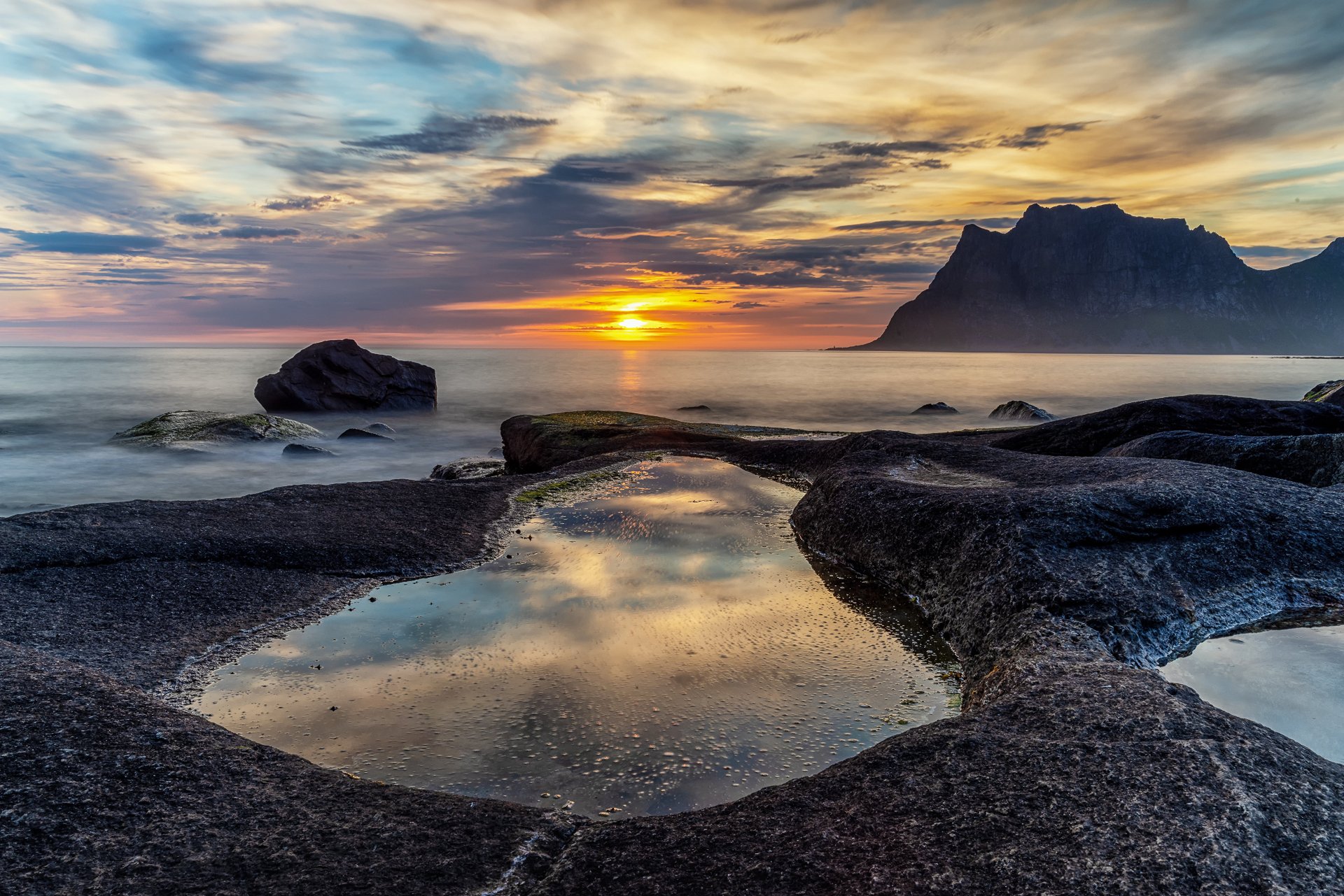 4K Ultra HD PC desktop wallpaper: Norway shoreline at sunrise with rugged black rocks, tidal pools reflecting a colorful sky and a distant mountain on the horizon.