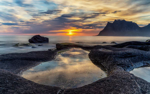 4K Ultra HD PC desktop wallpaper: Norway shoreline at sunrise with rugged black rocks, tidal pools reflecting a colorful sky and a distant mountain on the horizon.