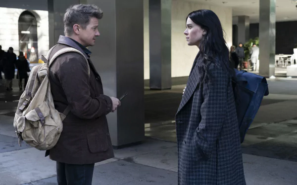 Hawkeye TV show 4K PC wallpaper: Kate Bishop and Clint Barton stand face-to-face in a dim urban plaza, both wearing coats and carrying backpacks.