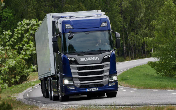Blue Scania R540 vehicle hauling a trailer on a winding forest road — 2K Quad HD PC desktop wallpaper/background.