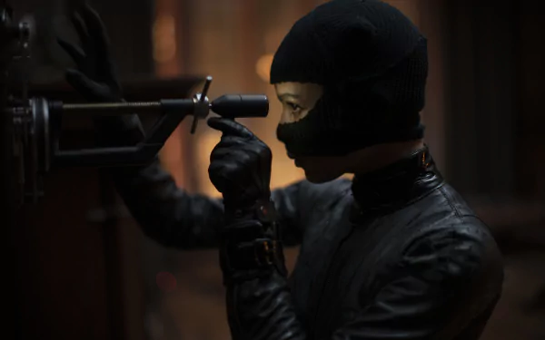 A masked character in black tactical gear manipulates a device in a dark setting, featured in an 8K Ultra HD PC desktop wallpaper from the movie The Batman.