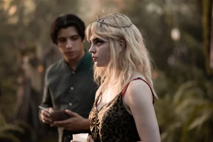 Yellowjackets TV show 4K wallpaper: pensive blonde woman with twig crown and patterned dress in a forest, a dark-haired man with a notebook stands behind.