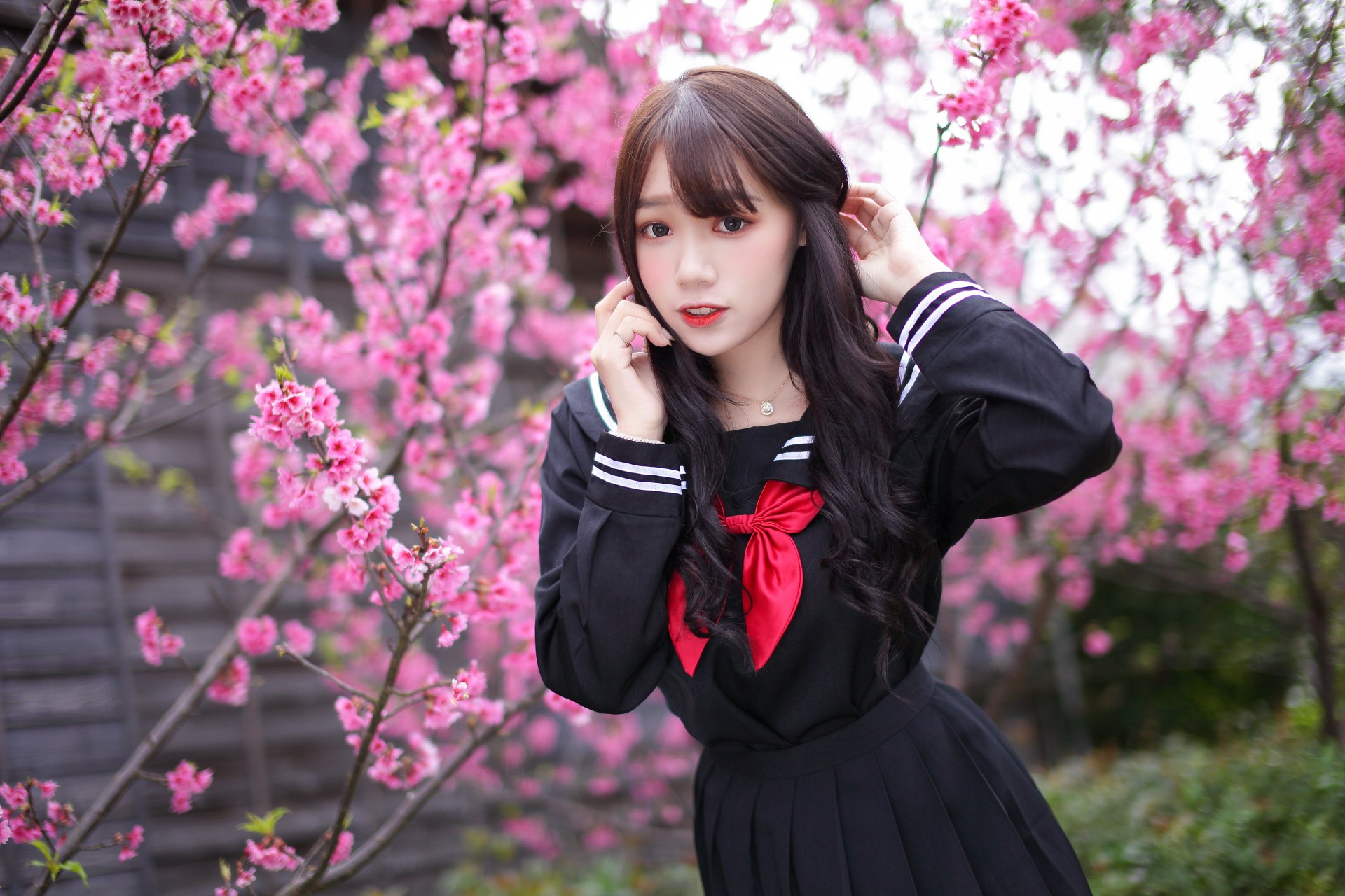 Brunette Asian woman in a school uniform poses amidst vibrant pink cherry blossoms, captured in stunning 4K Ultra HD for a PC desktop wallpaper.