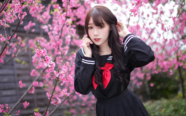 Brunette Asian woman in a school uniform poses amidst vibrant pink cherry blossoms, captured in stunning 4K Ultra HD for a PC desktop wallpaper.