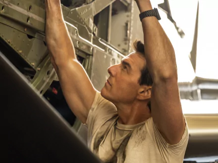 HD PC desktop wallpaper featuring Tom Cruise in a scene from the movie Top Gun: Maverick, working intently inside an aircraft.