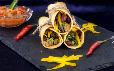 HD desktop wallpaper featuring a delicious burrito set on a slate surface, garnished with red chili peppers and yellow cheese strands, with a side of salsa.