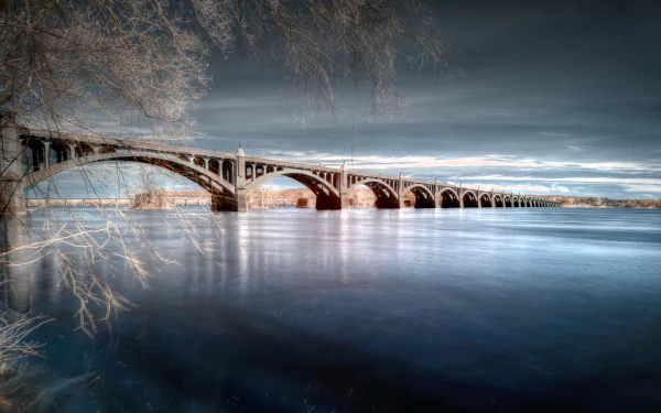 4K Ultra HD PC desktop wallpaper and background: a man-made arched bridge stretching across calm water beneath a moody, clouded sky.
