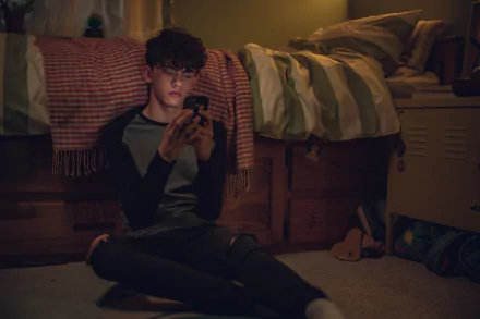 4K Ultra HD wallpaper from the TV show Heartstopper, featuring a young man sitting on the floor in a dimly lit bedroom, focused on his phone.