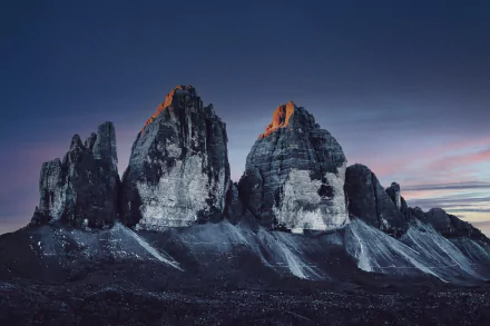 HD desktop wallpaper depicting the rugged peaks of Tre Cime di Lavaredo under a clear twilight sky, showcasing the natural beauty of this iconic mountain formation.