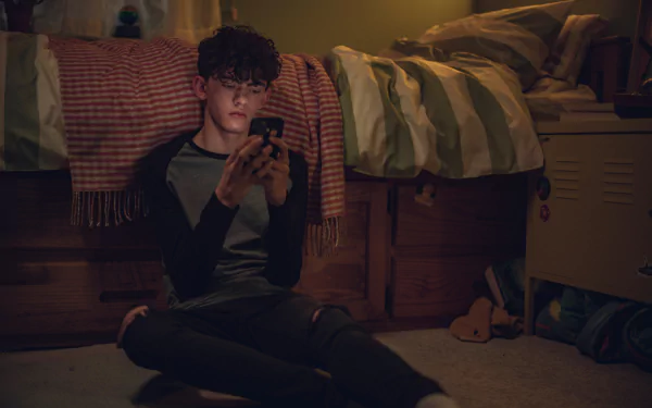 4K Ultra HD wallpaper from the TV show Heartstopper, featuring a young man sitting on the floor in a dimly lit bedroom, focused on his phone.